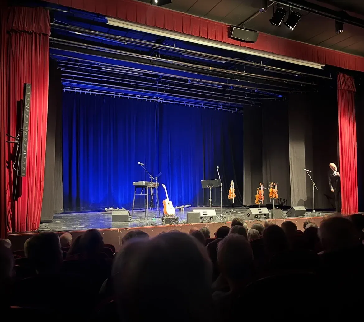 Föreställning på scen med musiker och röda draperier
